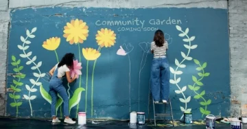 Two people painting a colorful flower mural on a wall.