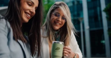 Two smiling women. One is holding a large green mug with a healthcare logo.