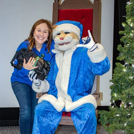 employee holding team holiday gift and posing with company mascot