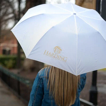 Person walking with branded Harding University umbrella