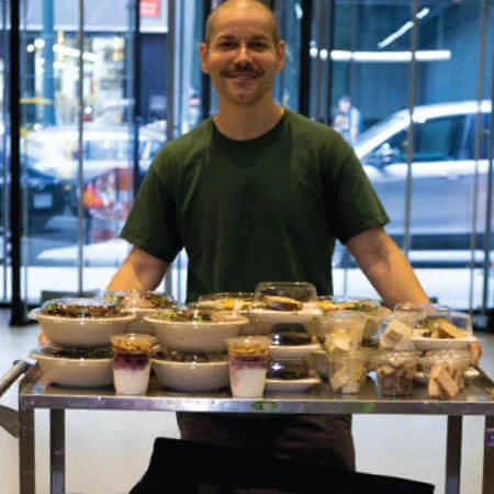 volunteer with Rescuing Leftover Cuisine standing next to a table filled with donated fresh food