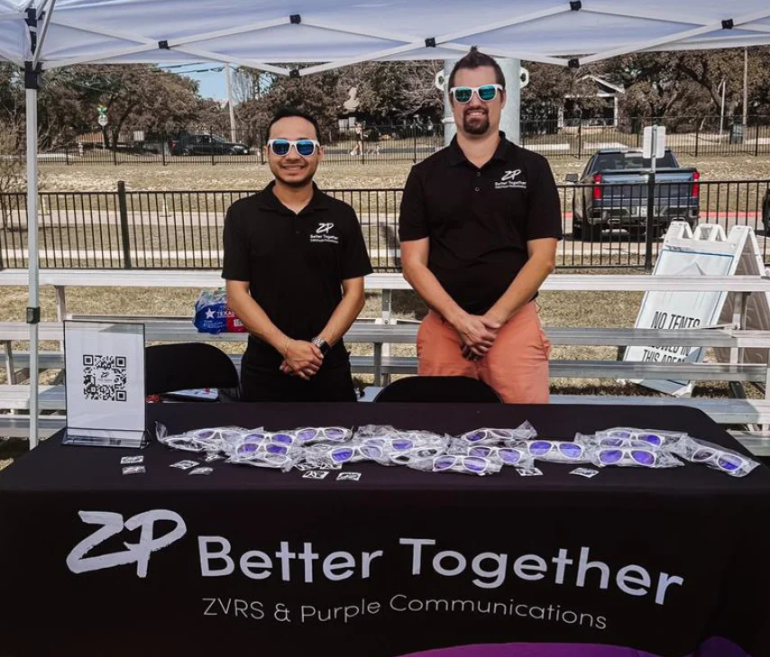 two people standing at a swag table wearing promo sunglasses