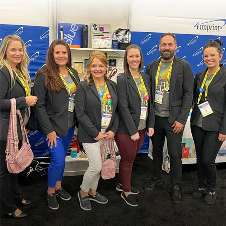 4imprint team pose for a picture with trade show promo products at their booth