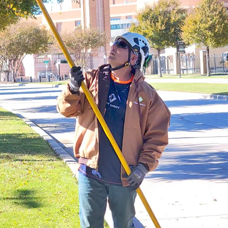 person wearing a logoed company jacket trimming trees