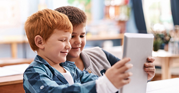 Two students playing a game on a digital tablet at school.