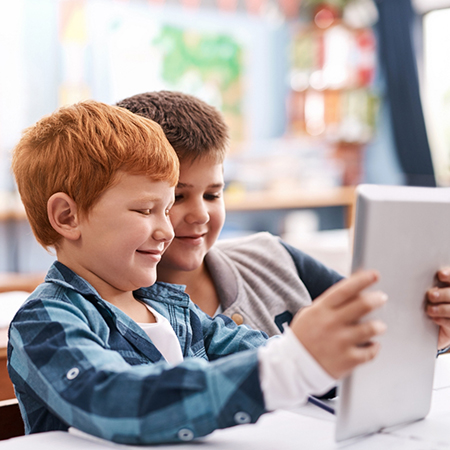 Two students playing a game on a digital tablet at school.