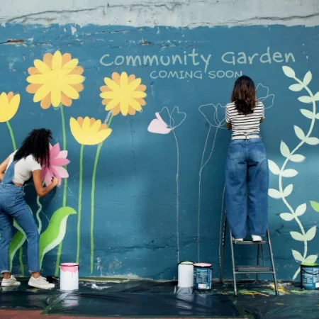 Two people painting a colorful flower mural on a wall.