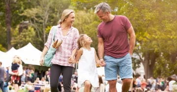 Smiling family holding hands and walking at an outdoor event.