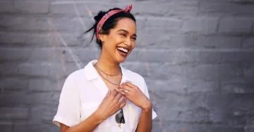 Happy person wearing a red bandana is standing in front of a gray wall.